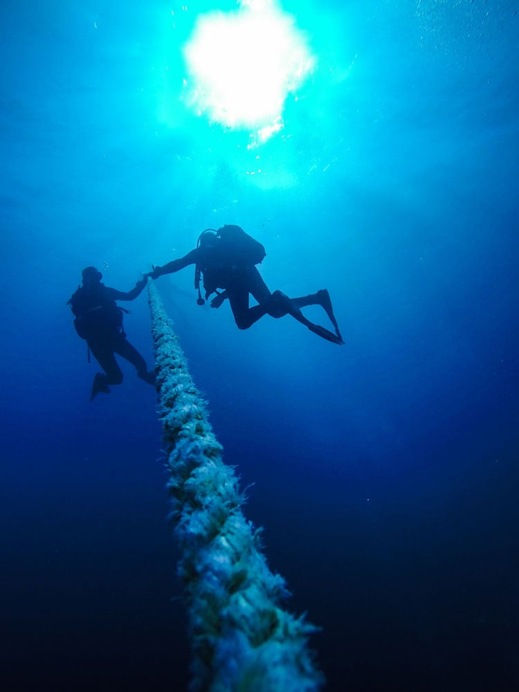 Scuba Divers Descending Holding a Rope to a Shipwreck in the Red Sea in Egypt